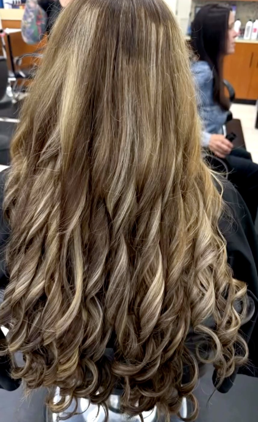 Long brown hair with balayage highlights styled in soft curls.