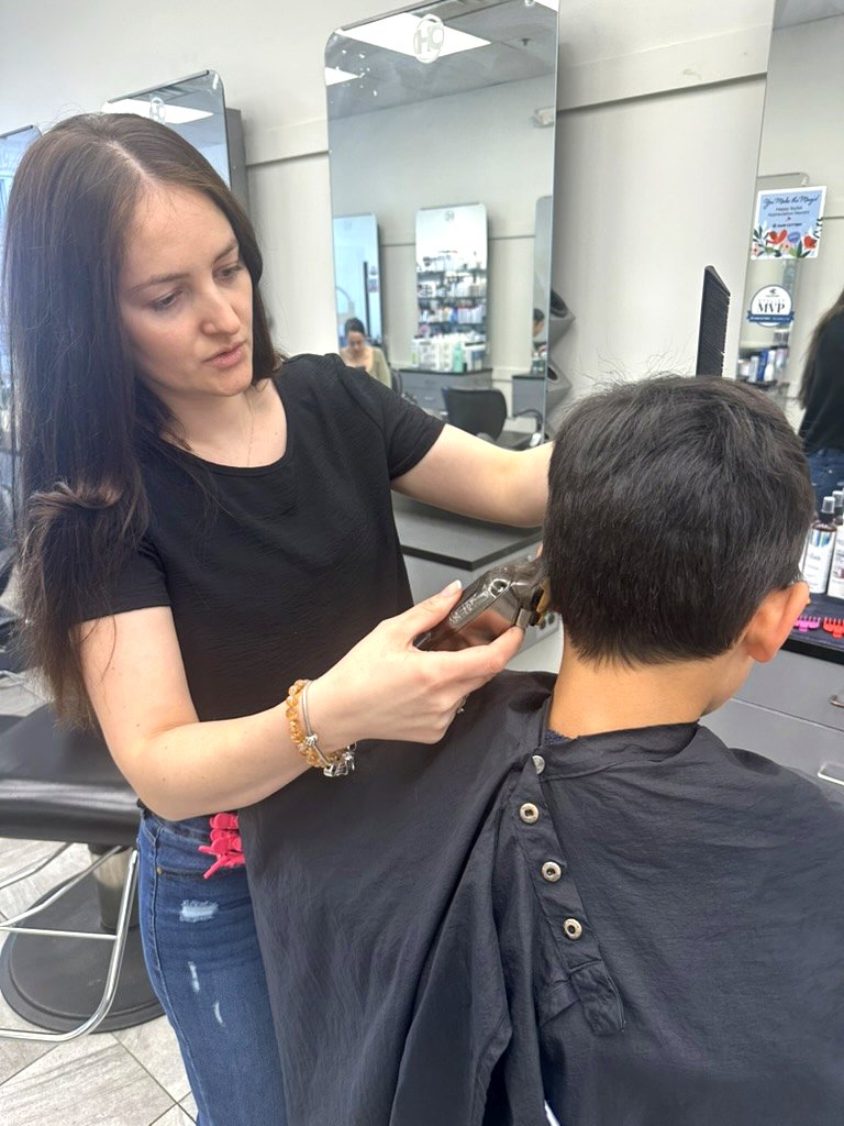 Ornela giving a young client a clipper haircut at her styling station.