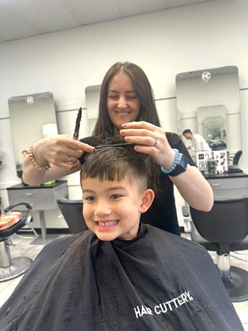 Ornela smiling with a young boy during his haircut.